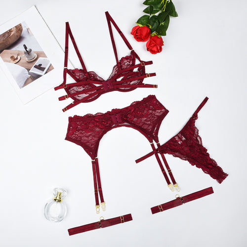 Flat lay presentation of the complete KissKismet 4-piece crimson desire set, including the peek-a-boo bra, high-waisted garter, thong, and leg harnesses.