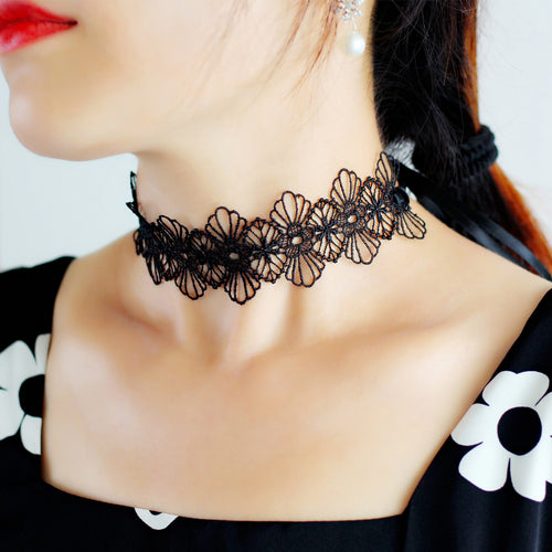 A side profile of a model wearing a delicate black hollow-out floral lace choker necklace, highlighting the collarbones and styled with a black and white garment.