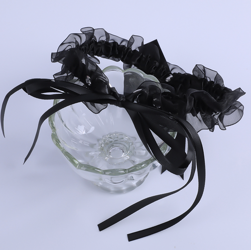 A black maid roleplay bell choker styled around a clear glass, showcasing its sheer mesh texture and adjustable ribbon ties.
