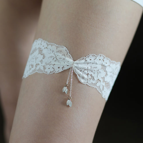 Close-up on-body view of the intricate white floral lace, central twisted knot, and shimmering chain fringe tassels on the Arachne Elysian bridal garter.