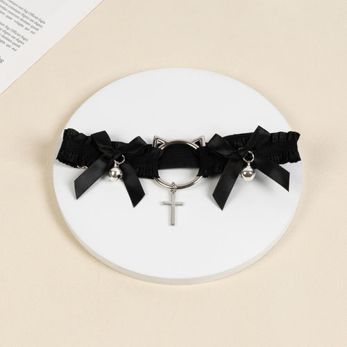 Flat lay view of the black ruffled thigh garter displaying the silver cat-ear hardware, ribbon bows, and cross pendant.