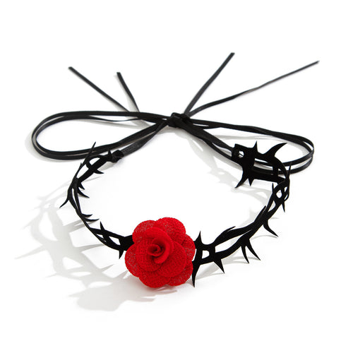 Flat lay view of the black thorn thigh garter with a red rose centerpiece, tied in a bow on a white surface.