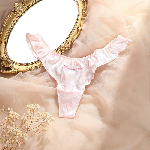 Romantic flat lay presentation of the KissKismet blush satin ruffled thong on a soft tulle background with a vintage gold mirror.