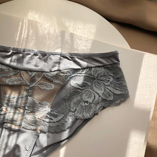 Close-up flat lay view of the KissKismet dusty blue panty bathed in sunlight, highlighting the delicate floral lace pattern and soft edges.