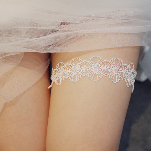 Front view of a white floral lace wedding garter with pearls worn on the thigh
