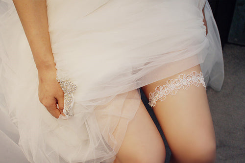 Bride lifting her white tulle wedding dress to reveal a delicate pearl and lace garter on her thigh