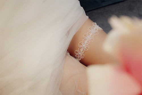 Soft focus view of a beautiful white lace and pearl bridal garter peeking from under a wedding gown