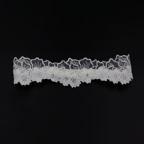 Flat lay front view of the white floral lace thigh garter against a contrasting black background.