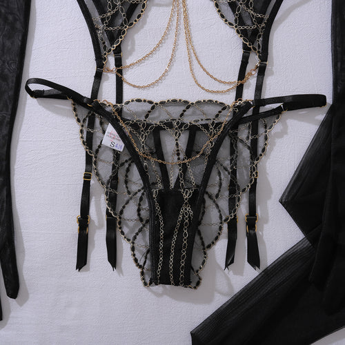 Close-up flat lay of the KissKismet gilded noir garter and thong, showing the exquisite gold-tone hardware and chain accents.