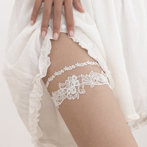 Close-up on-body view of a model wearing the white rose floral lace thigh garter underneath a white dress.