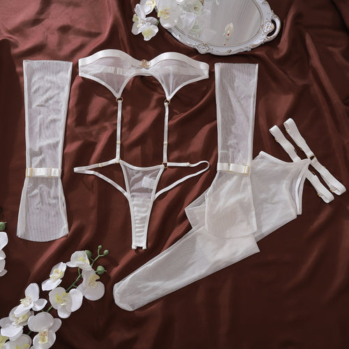 Flat lay presentation of the complete KissKismet ivory sheer mesh lingerie set on a brown satin background, featuring the cut-out teddy, sheer sleeves, and stockings.