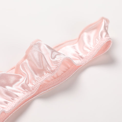 Detailed close-up of the lustrous blush pink satin fabric and delicate ruffled edges on the KissKismet coquette thong.