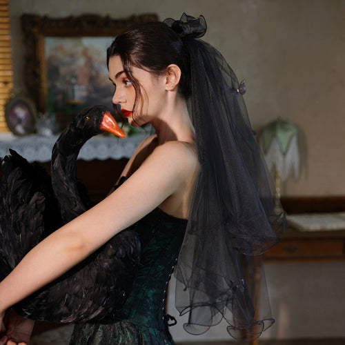Profile view of a model holding a black swan prop, styling the gothic short black veil.