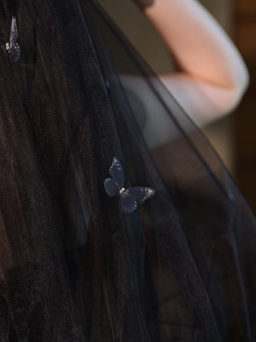 Extreme close-up of the delicate 3D butterfly applique resting on the sheer black tulle of the veil.