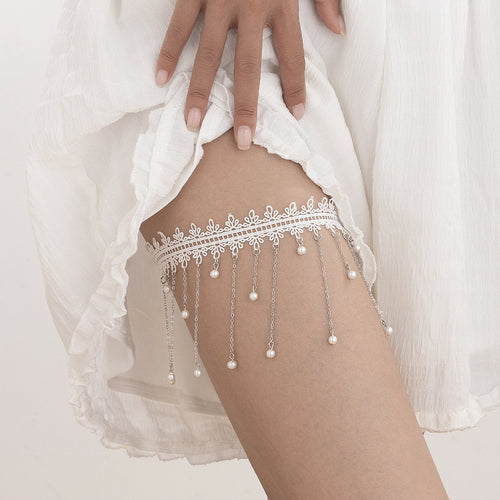 Front on-body view of a model wearing a white lace thigh garter featuring a cascading fringe of chains and pearls.