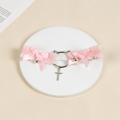 Flat lay view of the pastel pink ruffled thigh garter displaying the silver cat-ear hardware, ribbon bows, and cross pendant.