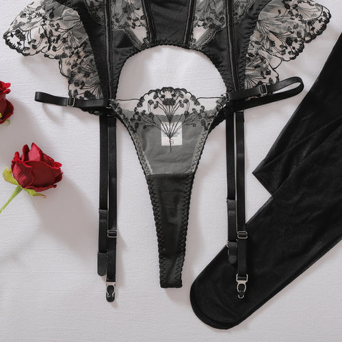 Close-up flat lay of the delicate ruffled garter belt, matching embroidered thong, and black stockings.