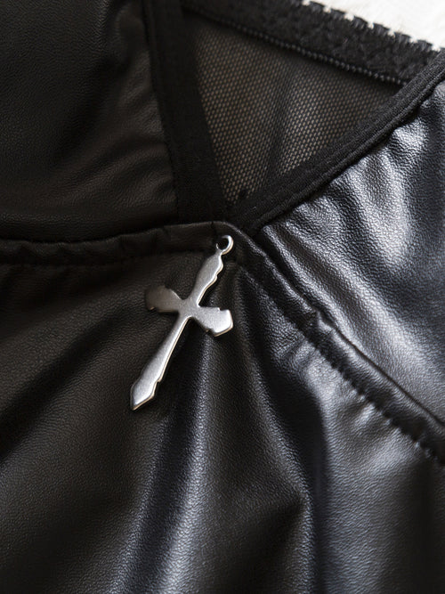 Extreme close-up detailing the striking silver cross pendant hardware and sleek faux leather texture on the KissKismet bodysuit.