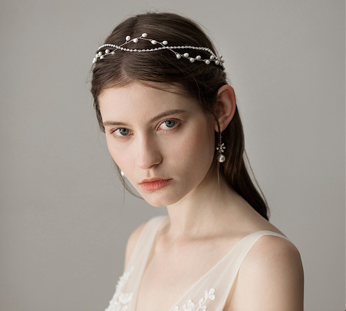 Close-up portrait of a bride wearing an intertwined silver pearl and rhinestone chain hair accessory.
