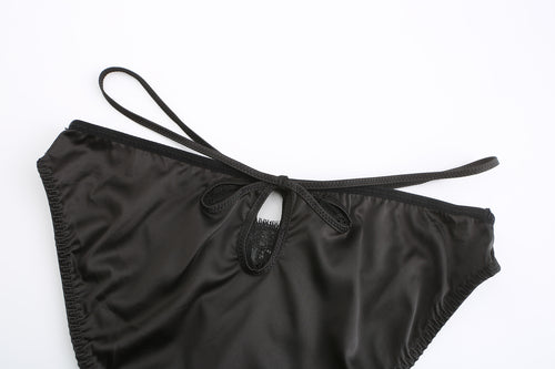 Flat lay of the matching KissKismet black satin thong, featuring a provocative front cut-out and strappy waist details.