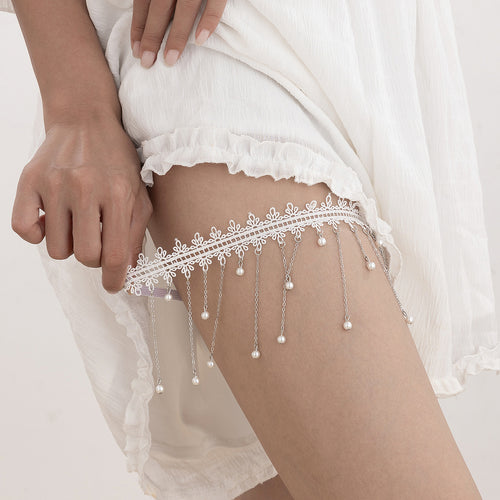 A model adjusting the delicate white lace and pearl fringe thigh garter, showing its stretchable fit.