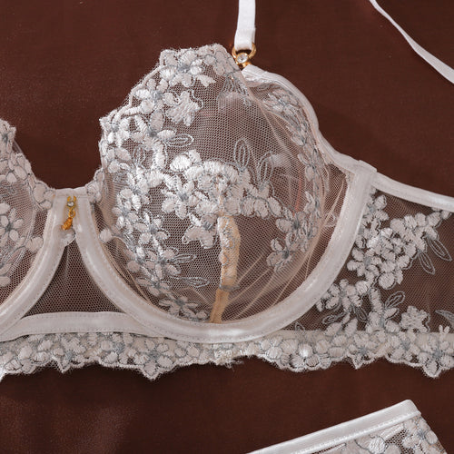 Flat lay detailing the matching white floral garter belt, strappy thong, and elegant sheer white thigh-high stockings.