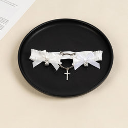 Flat lay view of the white ruffled thigh garter displaying the silver cat-ear hardware, ribbon bows, and cross pendant.