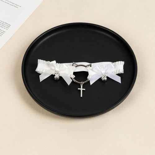 Flat lay view of the white ruffled thigh garter displaying the silver cat-ear hardware, ribbon bows, and cross pendant.