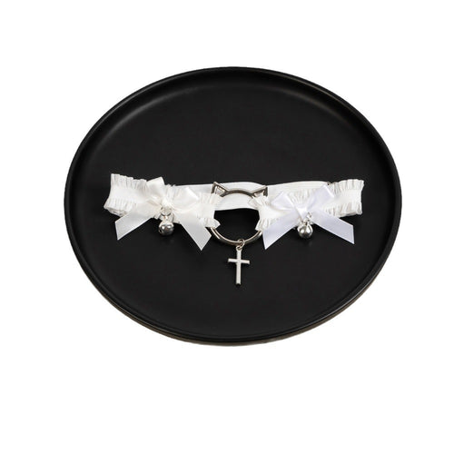 Top-down view of the white angelic thigh garter with bell and cross accents resting on a black surface.